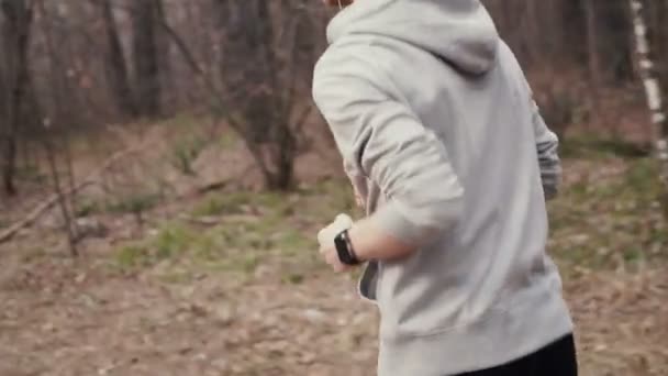 Hombre corriendo en bosques entrenando y mirando relojes inteligentes . — Vídeos de Stock