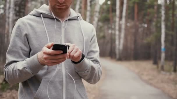 Joven corredor guapo con teléfono inteligente fuera en la naturaleza soleada otoño . — Vídeos de Stock