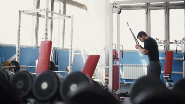 El hombre fuerte - el culturista con las mancuernas en el gimnasio, el ejercicio con la barra — Vídeo de stock