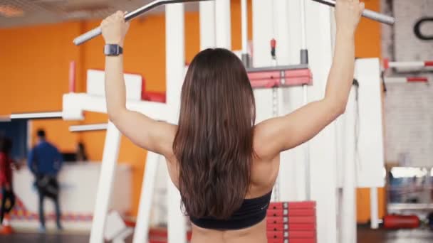 Mujer joven flexionando los músculos en la máquina de gimnasio por cable . — Vídeos de Stock