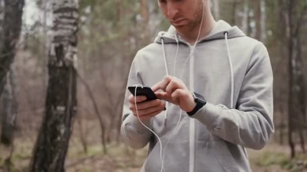 Młody przystojny biegacz z inteligentny telefon poza w słoneczny jesień natura. — Wideo stockowe