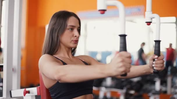 Mujer joven flexionando los músculos en la máquina de gimnasio por cable . — Vídeos de Stock