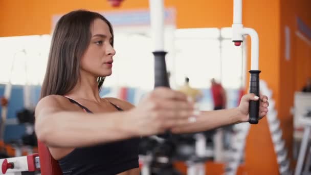 Mujer joven flexionando los músculos en la máquina de gimnasio por cable . — Vídeos de Stock