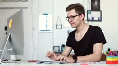 Mutlu genç adam, gözlüklü ve smiling, o onun laptop üzerinde çalışıyor