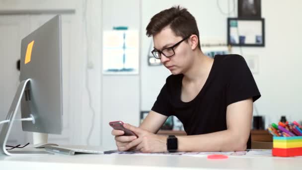 Молодий чоловік працює з дому за допомогою смартфона і ноутбука — стокове відео