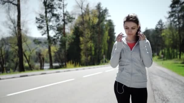 Schöne junge Läuferin setzt ihre Kopfhörer während des Trainings ein — Stockvideo