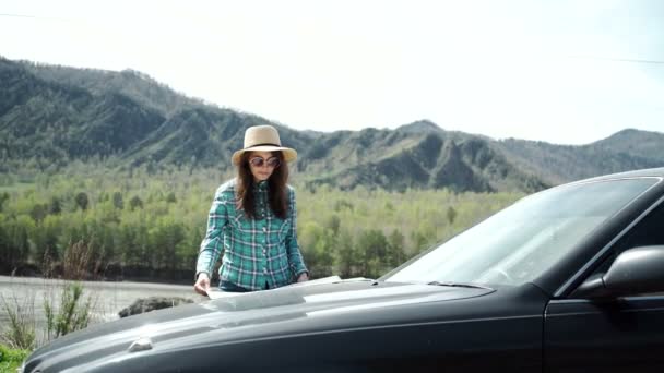 Подорожі - молода жінка з машиною дивиться на дорожню карту на пляжі проти моря і неба — стокове відео