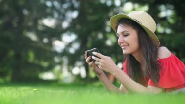 Yeşil çim üzerinde yalan boş kırmızı ekran ile cep telefonu kullanan genç kadın.