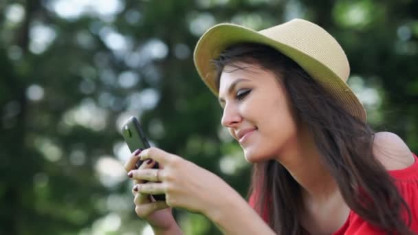 Mujer joven usando el teléfono móvil con la pantalla roja vacía acostada en la hierba verde . — Vídeo de stock