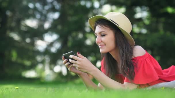 Mujer joven usando el teléfono móvil con la pantalla roja vacía acostada en la hierba verde . — Vídeos de Stock