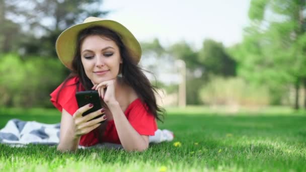 Young woman using mobile phone with empty red screen lying on the green grass. — Stock Video