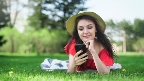 Young woman using mobile phone with empty red screen lying on the green grass. — Stock Video