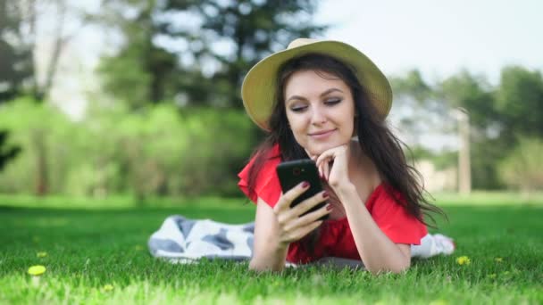 Jovem usando telefone celular com tela vermelha vazia deitada na grama verde . — Vídeo de Stock