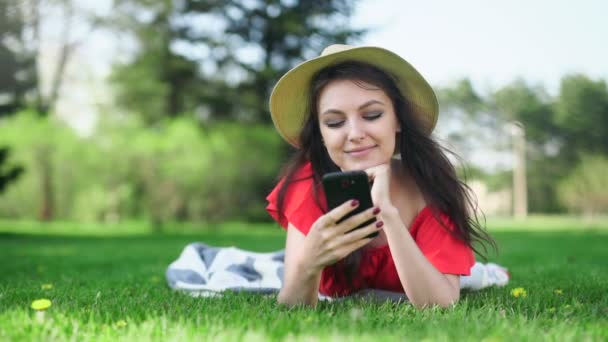Молодая женщина с помощью мобильного телефона с пустым красным экраном лежит на зеленой траве . — стоковое видео