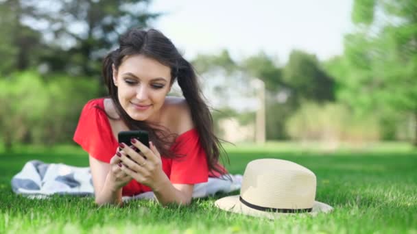 Young woman using mobile phone with empty red screen lying on the green grass. — Stock Video