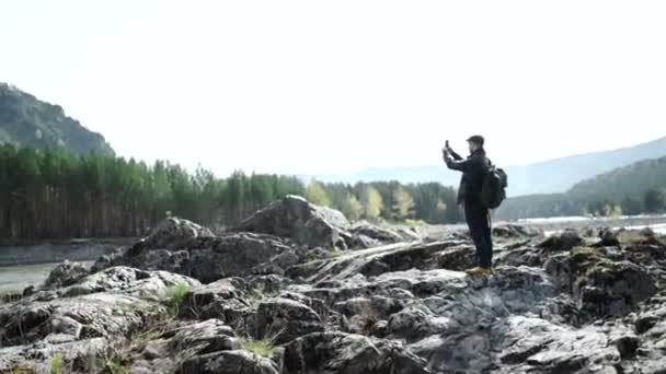 Hombre guapo haciendo foto en el teléfono inteligente al aire libre con el río en el fondo — Vídeo de stock