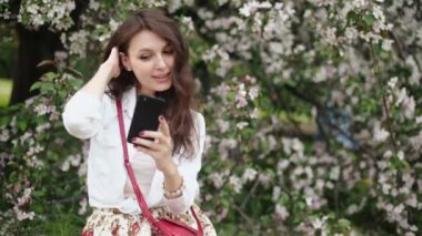 çayır çiçek açan ağacının üzerinde duran, smartphone kullanarak kadın