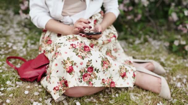 Çayır çiçek açan ağacının üzerinde duran, smartphone kullanarak kadın — Stok video