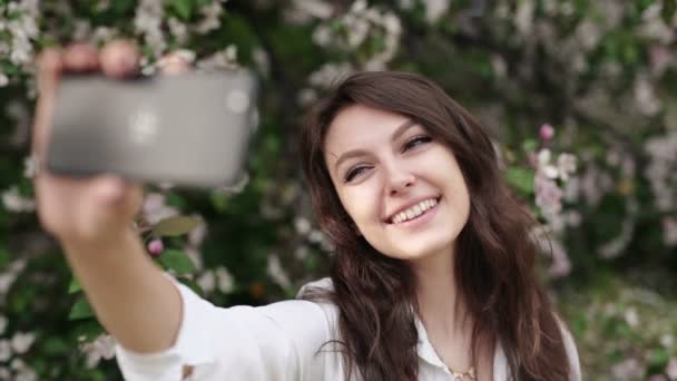 Щаслива жінка бере селфі на планшет у квітучому саду . — стокове відео