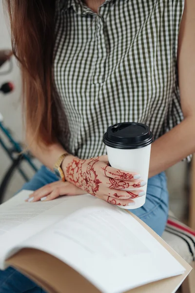 Young woman sipping coffee or tea and reading magazine