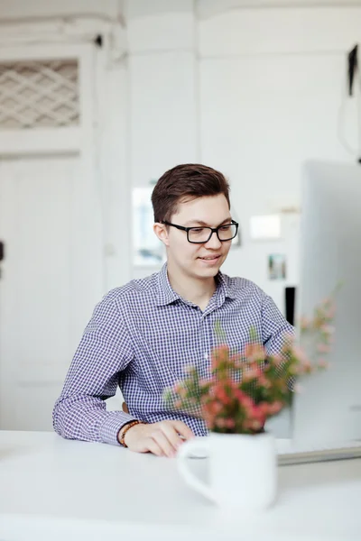 Jovem feliz, usando óculos e sorrindo, enquanto trabalha em seu laptop — Fotografia de Stock