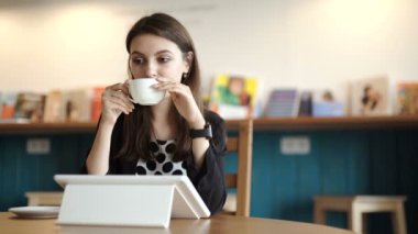 kadın bir restoranda bir masada oturur. Internet erişimi olan bir tablet taşıdı