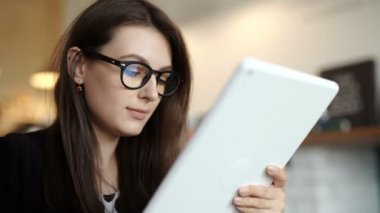 kadın bir restoranda bir masada oturur. Internet erişimi olan bir tablet taşıdı