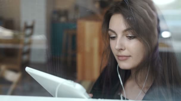 Fiatal nő segítségével tabletta coffee shop-val a fejhallgató — Stock videók