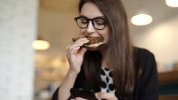 Café ciudad estilo de vida mujer en teléfono comer sándwich — Vídeos de Stock