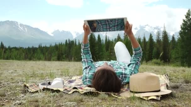 若い女性の屋外の芝生の上に敷設のタブレットを使用して笑顔 — ストック動画