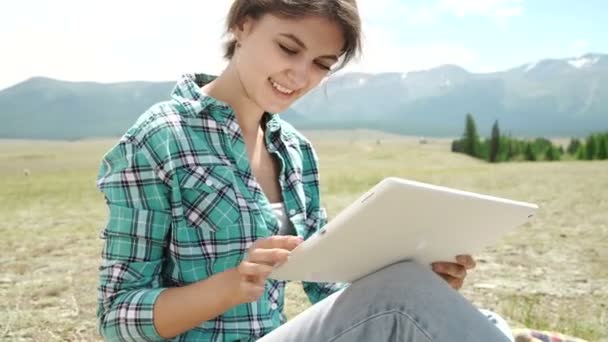 Jonge vrouw met behulp van Tablet PC buiten opleggen van gras, glimlachend — Stockvideo