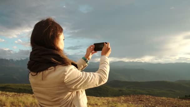 Молодая женщина-путешественница на фоне гор фотографирует на мобильный телефон. Изображение с ретро фильтром — стоковое видео