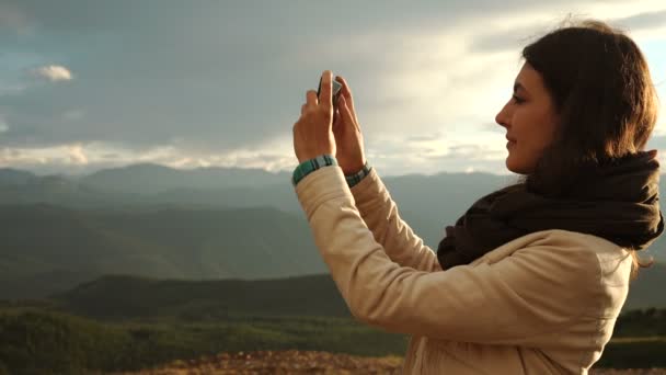 Eine junge Reisende vor dem Hintergrund der Berge macht Fotos mit dem Handy. Bild mit Retro-Filter — Stockvideo