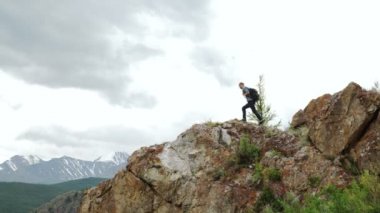 Sırt çantalı bir yürüyüşçü dağın tepesinde duruyor, elleri havada ve güneşin doğuşunun keyfini çıkarıyor.