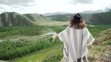 Dağları ile hill ve çevresindeki tepeler üzerinde rahatlatıcı panço ve şapka giyen genç güzel kadın Gezgin