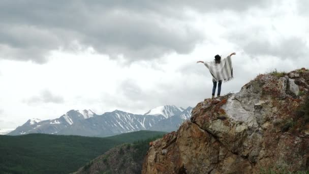 Joven mujer hermosa viajero con sombrero y poncho relajante en la cima de la colina con montañas y colinas alrededor — Vídeos de Stock