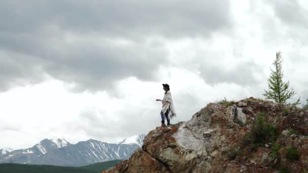 Young beautiful woman traveler wearing hat and poncho relaxing on the top of the hill with mountains and hills around — Stock Video