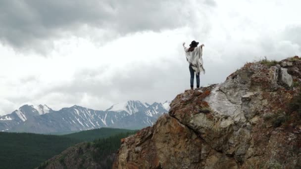 Jovem mulher bonita viajante vestindo chapéu e poncho relaxante no topo da colina com montanhas e colinas ao redor — Vídeo de Stock