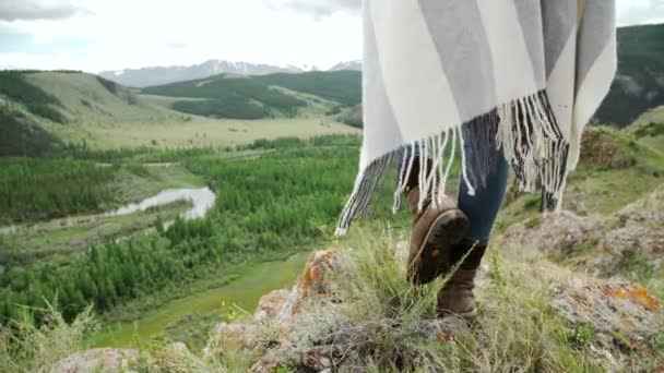 Young beautiful woman traveler wearing hat and poncho relaxing on the top of the hill with mountains and hills around. — Stock Video