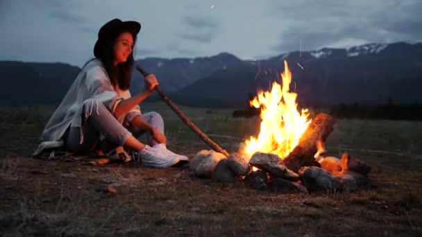 La chica en un suéter caliente sentado junto al fuego en la noche . — Vídeos de Stock