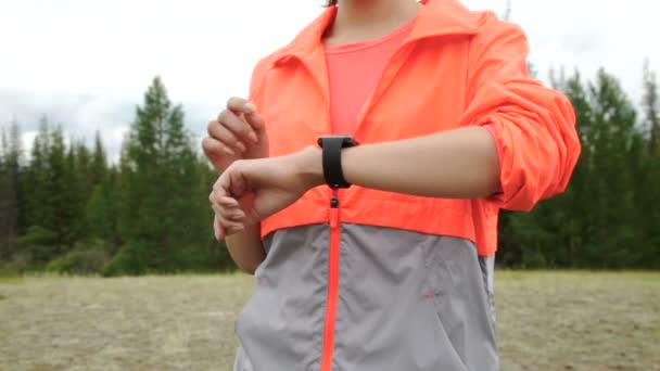 Runner using smartwatch fitness tracker and heart rate monitor watch jogging on trail in forest. Female athlete checking her cardio training data during workout outside in running park. — Stock Video