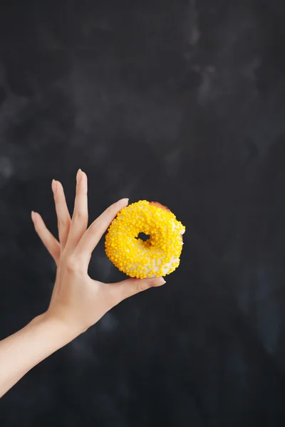 Rosquilla amarilla en una mano de mujer sobre fondo negro —  Fotos de Stock