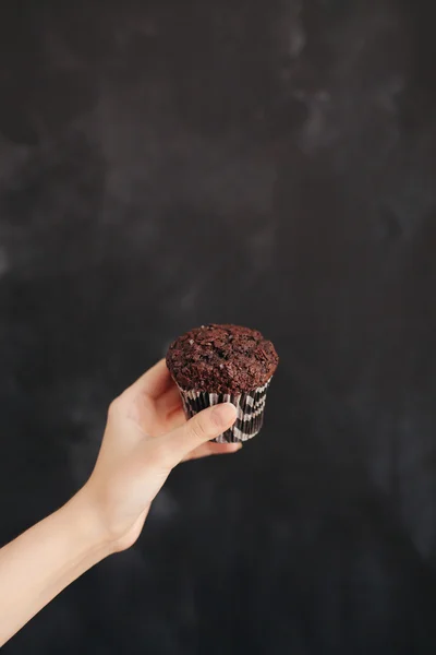 Жінка тримає шоколадний кекс на чорному тлі — стокове фото