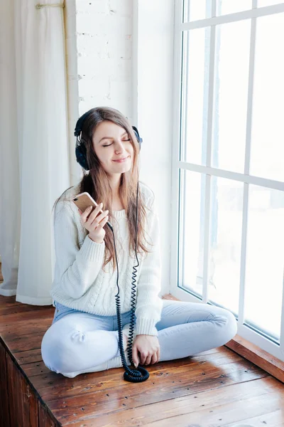 Nő zenehallgatás fejhallgató ablakpárkányon háttér — Stock Fotó