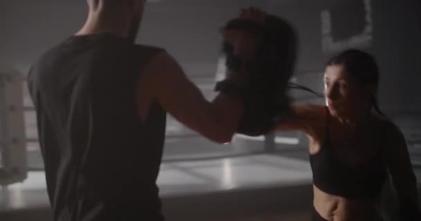 Giovane atleta donna in guanti da boxe e abbigliamento sportivo è boxe con il suo abile allenatore. Schivano pugni mentre si esercitano sul ring di boxe. — Video Stock