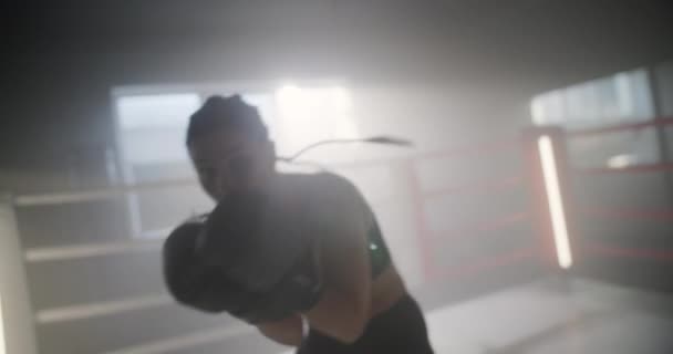 Kobieta trenuje boks w ringu bokserskim. Kobieta Fighter zadaje ciosy i patrzy w kamerę w Dark Ring. Portret kobiety Kickboxer. Koncepcja boksu. — Wideo stockowe