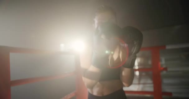 ボクシングリングの女性トレーニングボクシング。女戦士はパンチをスローし、暗いリングでカメラを見て.女キックボクサーの肖像画。ボクシングのコンセプト. — ストック動画