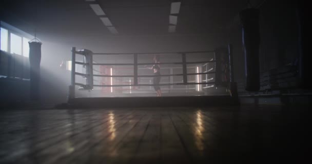Junge Boxerin springt mit in Binde gewickelten Händen auf Seil im dunklen Ringraum einer Sporthalle mit Rauch. — Stockvideo