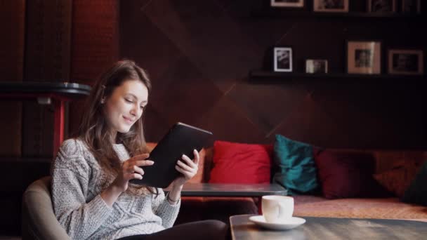 Mujer joven bebiendo café y el uso de la tableta en una cafetería — Vídeos de Stock