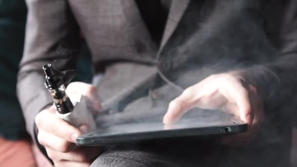 Бизнесмен с электронной сигаретой и читает свой планшетный компьютер — стоковое видео